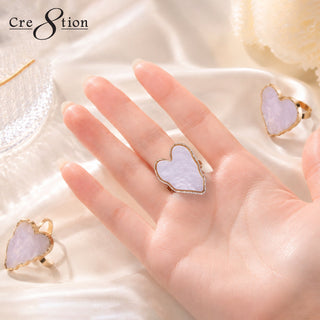 Open palm wearing a lilac heart shaped Cre8tion mixing ring palette, two more rings on white silk.