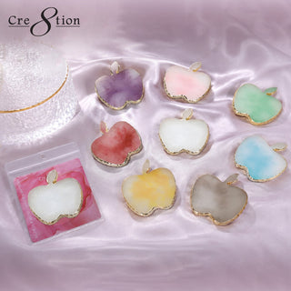 Apple shaped Cre8tion palettes with gold rims in purple, pink, white, red, green and blue on lilac silk.