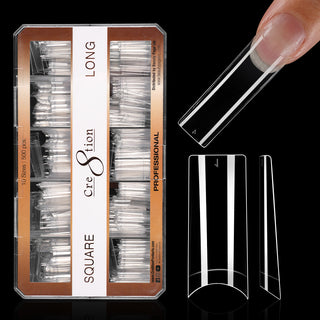 Kraft box of clear Cre8tion square tips on black, long length, with one tip worn on a fingertip.
