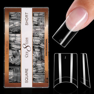 Kraft box of clear Cre8tion square tips on black, short length, with one tip worn on a fingertip.