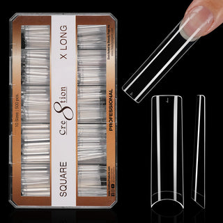 Kraft box of clear Cre8tion square tips on black, extra long, with one tip worn on a fingertip.