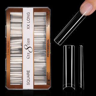 Kraft box of clear Cre8tion square tips on black, extra extra long, with one tip worn on a fingertip.