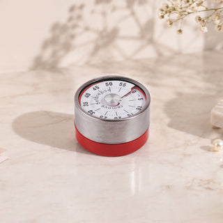 Round Cre8tion mechanical salon timer with a steel dial face and a red base, on marble.